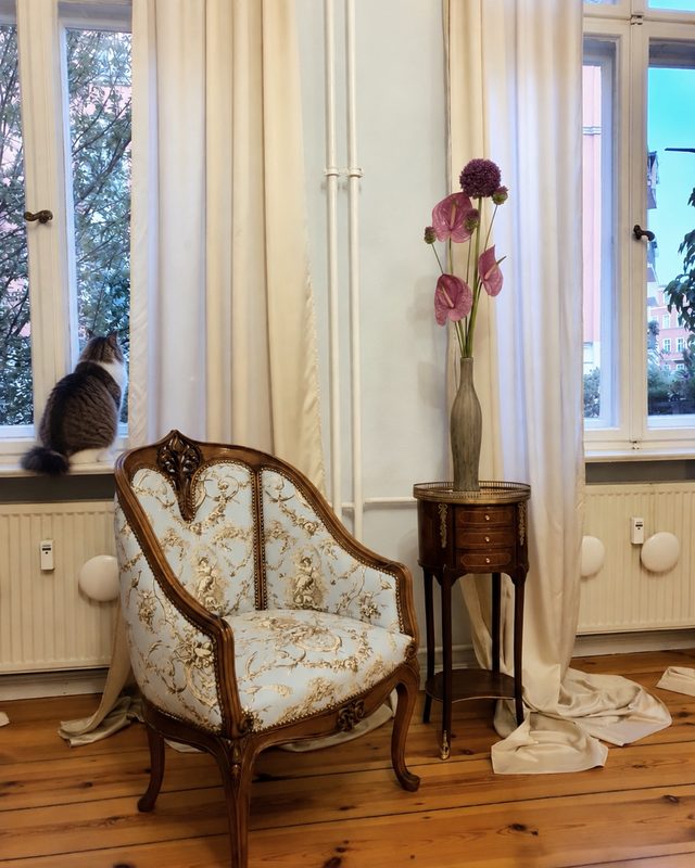 Upholstered armchair and small side table in front of a period-building window